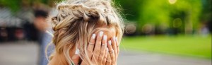 Woman with her hair done up with her hands covering her face outside.